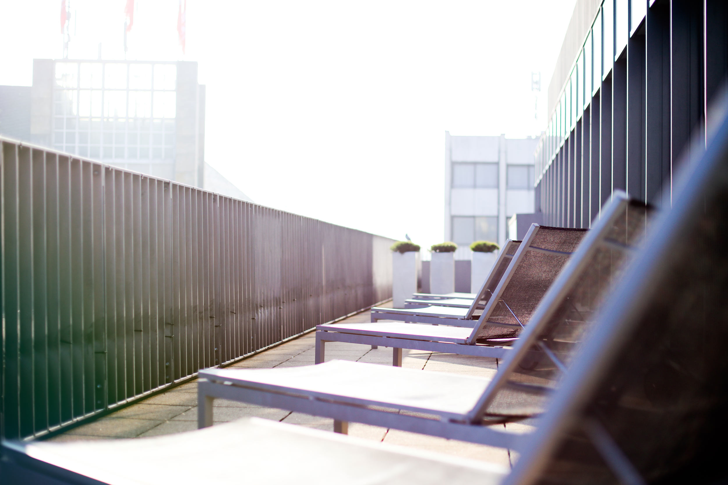 Zu sehen ist ein Bild einer Sonnenterrase mit Liegen. Das Bild hat den Fluchtpunkt in der Mitte und es sind mehrere Sonnenliegen versetzt zu erkennen. Die sonne scheint im oberen Teil dieses Bildes und erzeugt einen insgesamt hellen Eindruck.